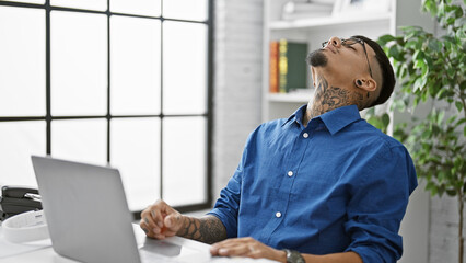 Fototapeta premium Stressed young latin business worker, man sweating bullets overwork using laptop at office desk.