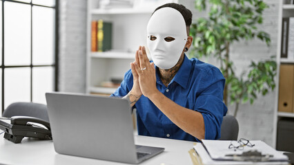 Young latin man hacking, a masked hacker tapping away on his laptop, eyes glued to the screen, poised in his office, ready to commit his next cyber crime