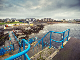 View on Salthill promenade from Blackrock diving board. Galway city, Ireland. Popular town landmark, loved by local swimmers and tourist for beautiful view. Cloudy sky.