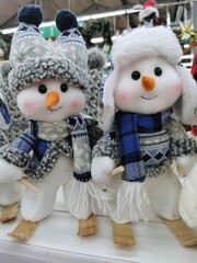 New Year's snowmen in blue scarves with ornaments stand on the store window, creating a cozy atmosphere of a Merry Christmas holiday