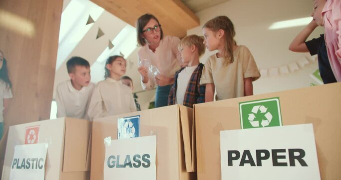 a blonde girl with a bob hairstyle teaches preschool children how to properly fold plastic bottles and sort garbage by type of material in a club to prepare children for school