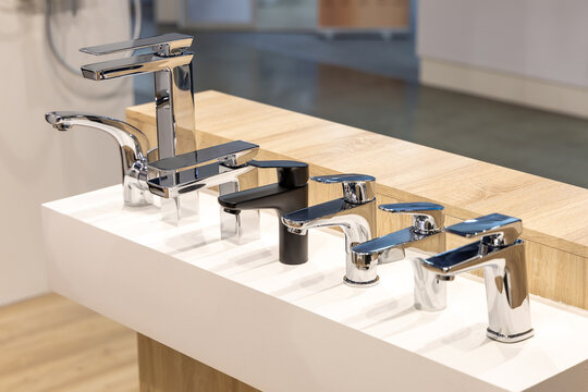 Modern sink faucets on a stand in a plumbing store or at an exhibition. Taps with shiny chrome surface and stylish design. White stand for convenient selection of faucets