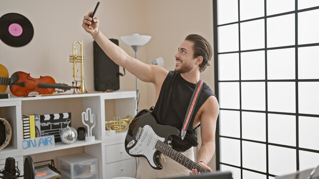 Young hispanic man musician playing electrical guitar make selfie by smartphone at music studio