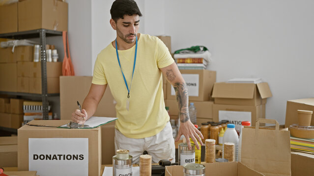 Young hispanic man volunteer writing on clipboard checking products at charity center