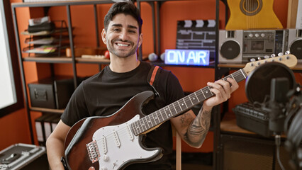 Young hispanic man musician smiling confident holding electrical guitar at music studio