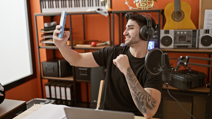 Young hispanic man musician sitting on table having video call at music studio