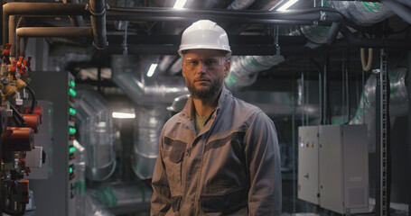 Male heavy industry worker wearing safety uniform, protective glasses and hard hat looks at camera....
