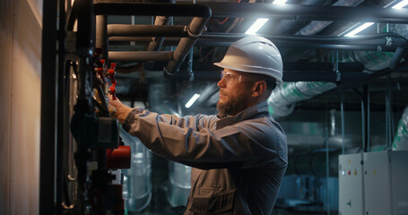 Male heavy industry worker wearing safety uniform, protective glasses and hard hat checks pipeline system. Engineer maintains modern manufacturing factory or industrial facility. Concept of industry.