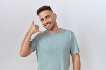 Hispanic man with beard standing over white background smiling doing phone gesture with hand and fingers like talking on the telephone. communicating concepts.