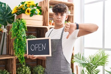 Hispanic teenager working at florist holding open sign with angry face, negative sign showing...