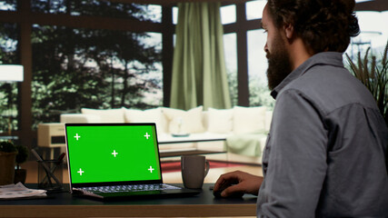Young millionaire checks greenscreen template on laptop, getting cozy in his extravagant mountain...