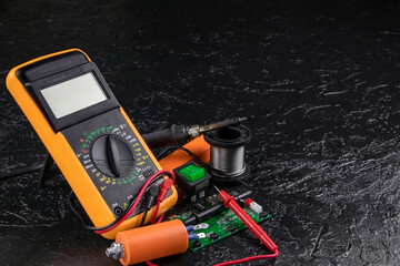 Digital multi-meter with probes on a black stone background. Multitester and microcircuit. Voltage Tester. Copy space. Voltmeter. Measuring tool. DMM.