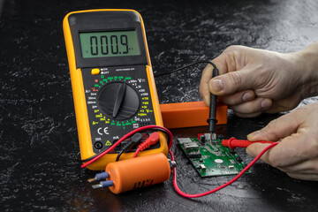 An electrician takes readings from a microcircuit using a multimeter. Measuring instruments. Voltage measuring tool. Checking battery voltage. Male hands repairing a microcircuit.