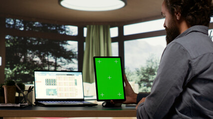 Company CEO examines greenscreen templates on tablet, working with modern gadgets at his...
