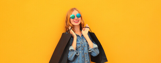 Stylish happy smiling young woman posing with shopping bags wearing denim jacket on yellow studio...