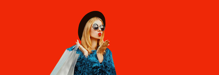Stylish woman with shopping bags blowing her lips sends air kiss with lipstick wearing blue fur...