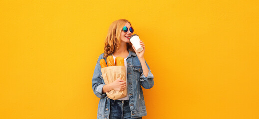 Portrait of happy smiling young woman holding grocery shopping paper bag with long white bread baguette and cup of coffee on orange background - obrazy, fototapety, plakaty
