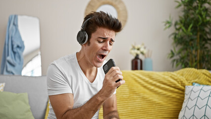 Fototapeta premium Young hispanic man singing song using smartphone as a microphone at home