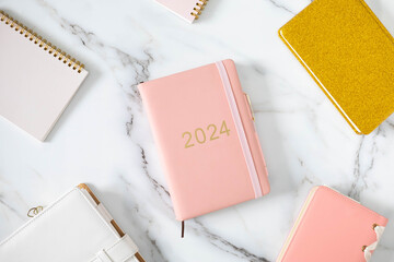 Pink coral colored diary for the year 2024 and many other diaries, pen, marble background