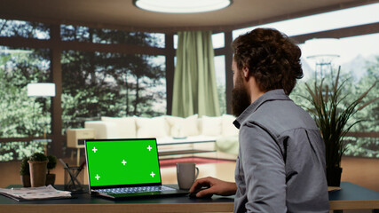 Wealthy investor relaxes in his elegant mountain chalet while looking at greenscreen display on his notebook. Foreign supervisor works with isolated mockup panel on laptop in prosperous life.