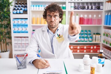 Hispanic young man working at pharmacy drugstore pointing with finger up and angry expression,...