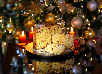 Italian Christmas cake Panettone with slices, on black glass against the background of a decorated Christmas tree