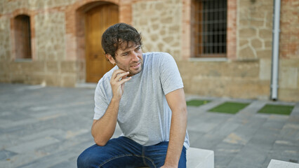 Cool, relaxed young guy with blond beard and handsome expression, sitting on park's bench, immersed...