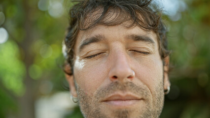 Hispanic young man with closed eyes, enjoying a breathing meditation in a sunny city park, a symbol...
