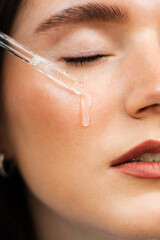 Attractive girl drops essential oil on facial skin close-up. Young woman is applying moisturizing serum on her face.