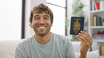 Happy young man, smiling and sitting at home on sofa, holding his canadian passport, ready for...