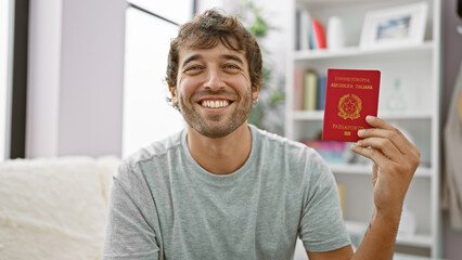Young man smiling holding passport of italy sitting on the sofa at home