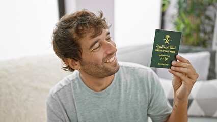 Confident, happy young arab man, lounging on the sofa at home, grinning ear to ear, while clutching...