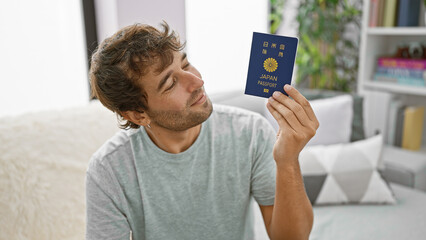 Confident young man, joy radiating from his smile, sitting casual on his sofa, holding passport,...