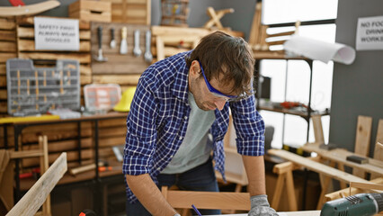 Handsome blond, young hispanic man, busy taking notes in his indoor workshop. carpentry is his...