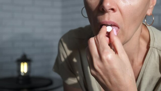 Sick lady eats a pill of vitamins. A view of sick female take a pill at home. A concept of use painkillers because of health problems.