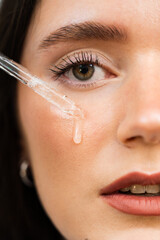 Young woman with acid dropper is applying drops of acid on her skin. Girl applying hyaluronic serum with pipette on face close-up.