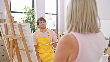 Fototapeta premium Two passionate artists man and woman joyfully choosing their paintbrushes for their next masterpiece at their beloved art studio