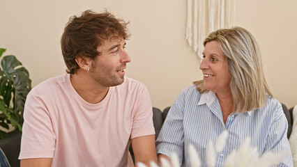 Heartwarming mother and son sitting together on the living room sofa, joyfully hugging and smiling in their cozy home, radiating happiness and confidence in their casual lifestyle.