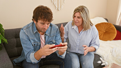 Angry mother and son engaged in heated debate over smartphone use, sitting upset on their living room sofa at home. the usual family love now replaced by a troublesome argument.