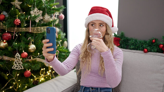 Young blonde woman celebrating christmas taking selfie picture smartphone drinking wine at home