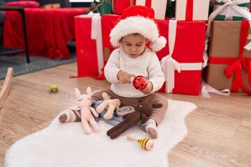 Adorable hispanic toddler holding christmas ball decoration sitting on floor at home