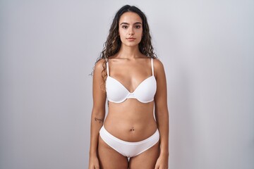 Young hispanic woman wearing white lingerie relaxed with serious expression on face. simple and natural looking at the camera.