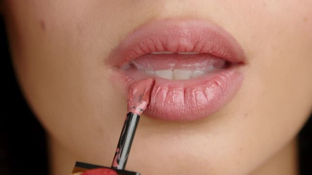 Female hand with red manicure applying lipstick of natural color with a brush on full upper and lower lips with mouth slightly open, smacking them sexually. High quality 4k footage
