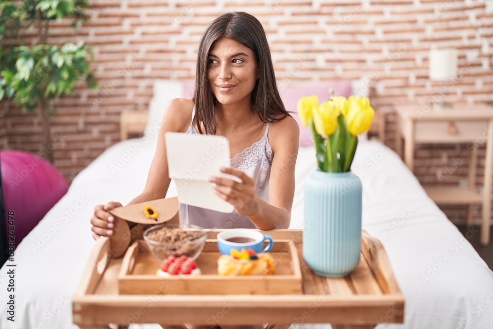 Poster brunette young woman eating breakfast in the bed reading a letter smiling looking to the side and st