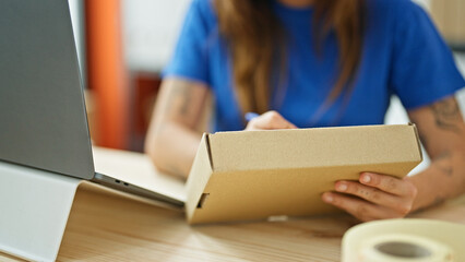 Young beautiful hispanic woman ecommerce business worker writing on package at office