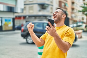 Young hispanic man using smartphone with winner expression at street