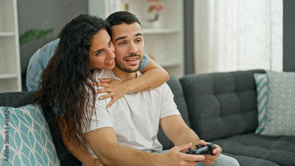 Poster man and woman couple playing video game sitting on sofa at home