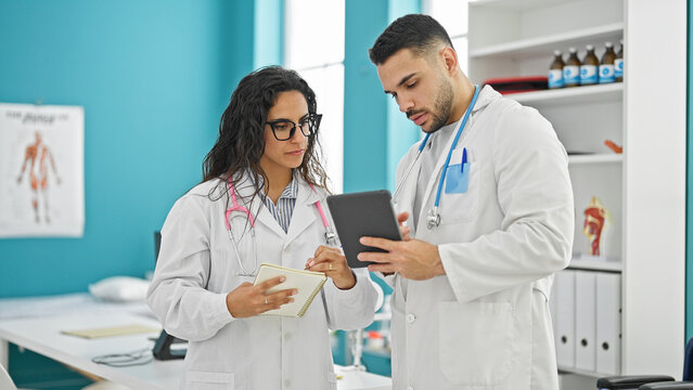 Man and woman doctors standing together using touchpad taking notes at the clinic
