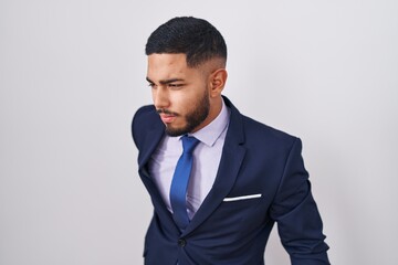 Young hispanic man wearing business suit and tie suffering of backache, touching back with hand, muscular pain