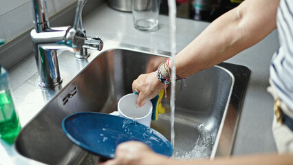 Middle age hispanic woman washing plates at the kitchen